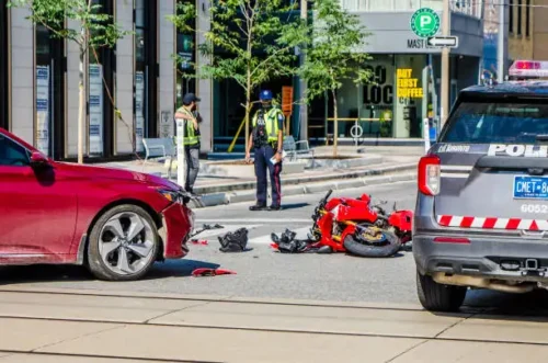 Toronto police officers at the scene of a motorcycle and car accident, with debris and emergency vehicles visible on the road.