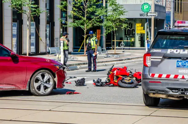 Toronto police officers at the scene of a motorcycle and car accident, with debris and emergency vehicles visible on the road.