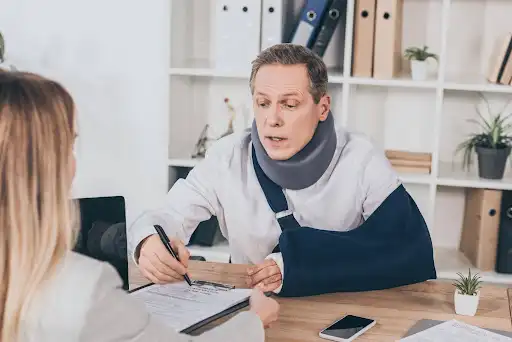 Injured Heart Lake resident with an arm sling signing papers at a personal injury lawyer’s office